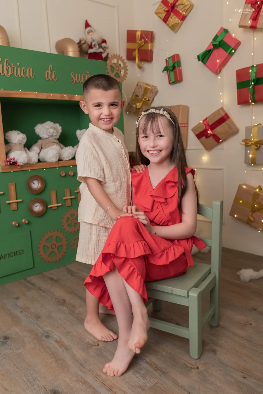 Hermanos abrazados en el set, frente a un mueble verde con regalos colgados