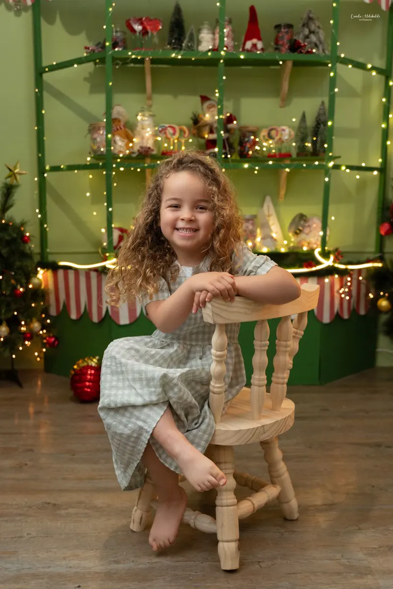Niña de rulos sentada en una sillita de madera frente a la estantería de dulces iluminada