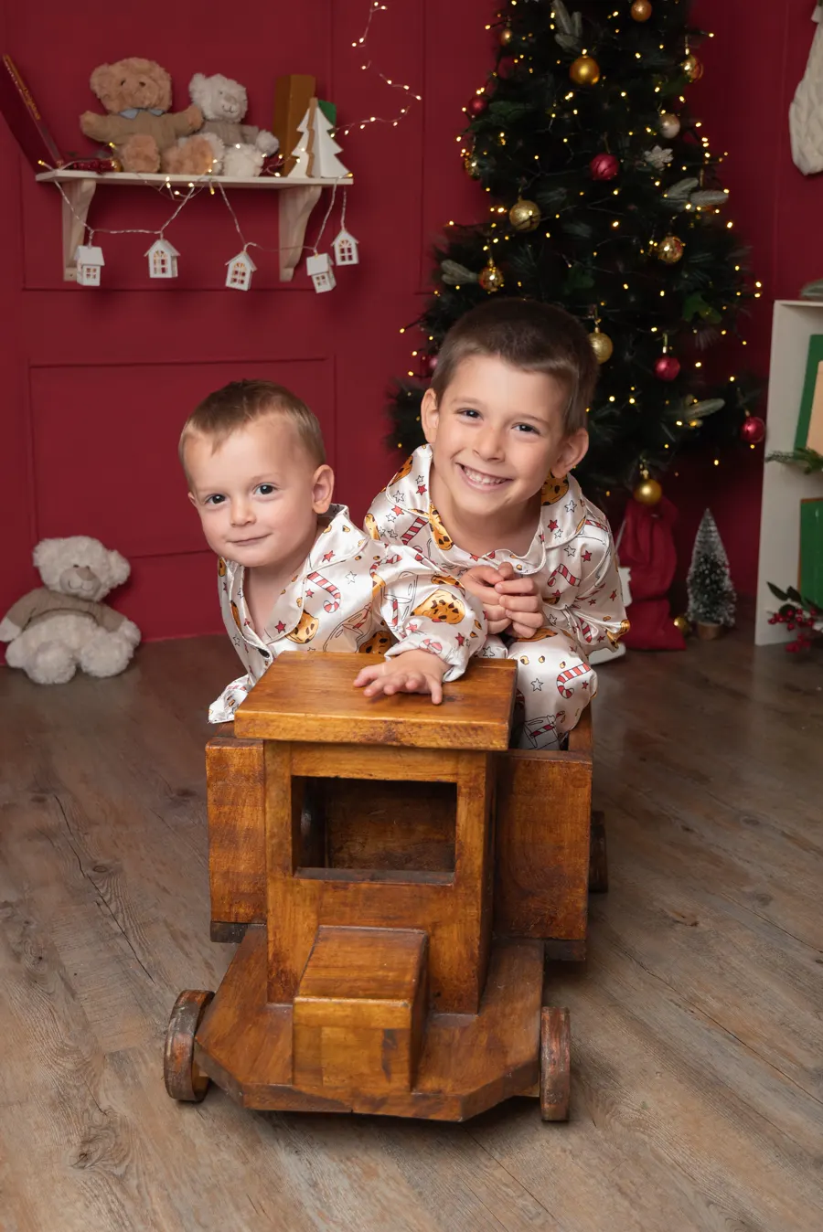 Dos hermanos en pijama navideño subidos a un trencito de madera junto al árbol